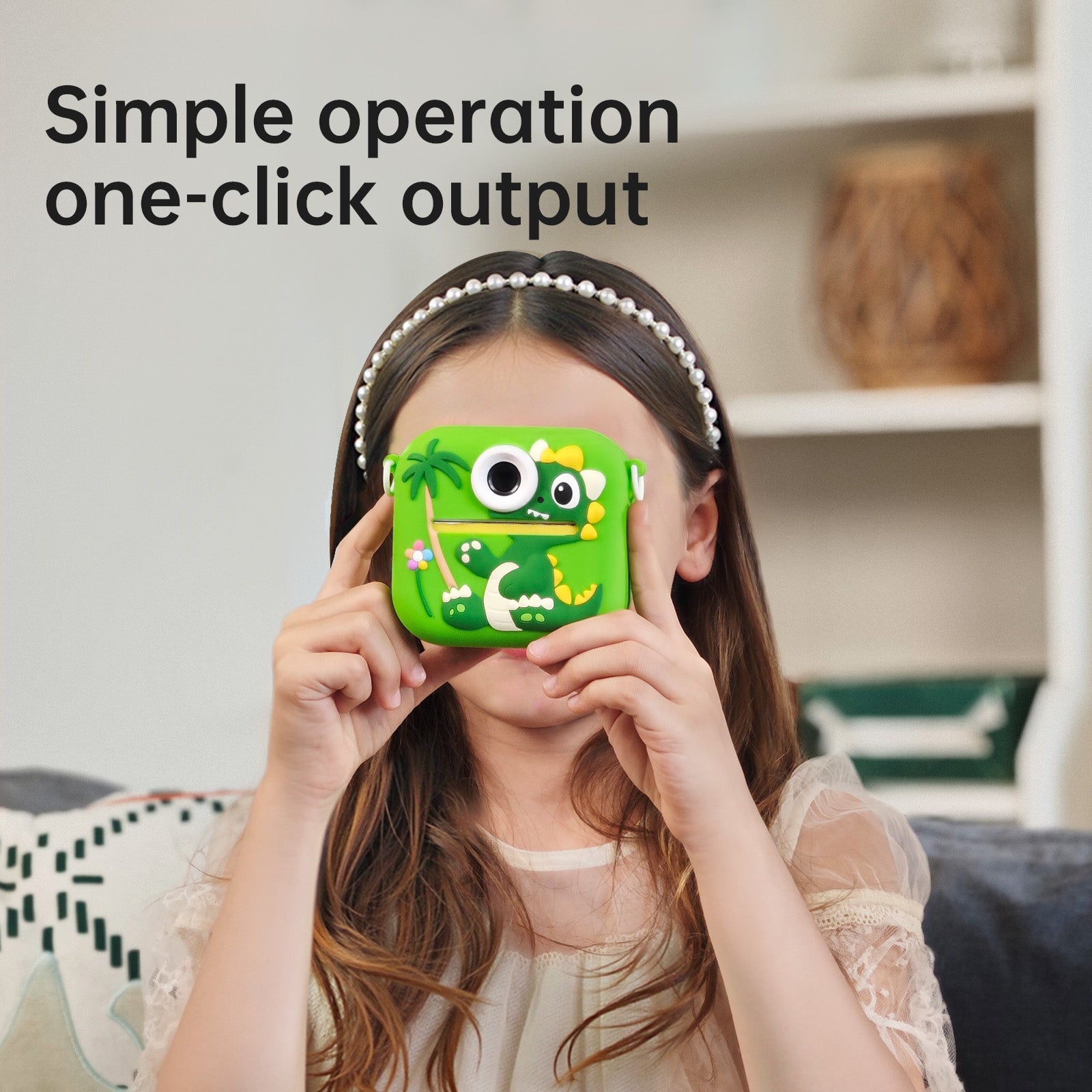A child wearing a pearl headband holds a bright green monster-shaped phone case in front of their face. The case has cartoon eyes, a smiling mouth, and tropical leaf details.